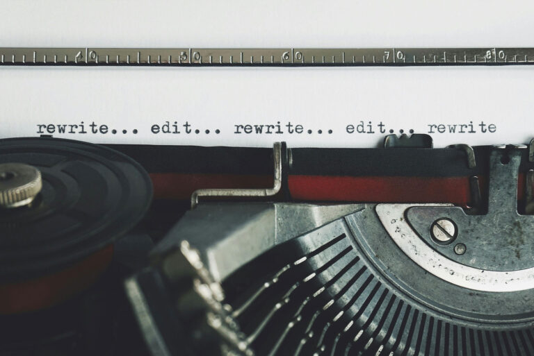 A close-up of a typewriter with a sheet of paper that reads “rewrite... edit... rewrite... edit... rewrite” in black type.