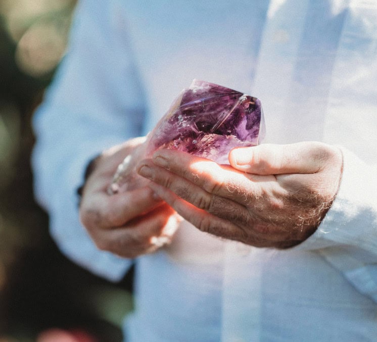 A person in a white shirt holds a large, polished purple crystal with both hands.