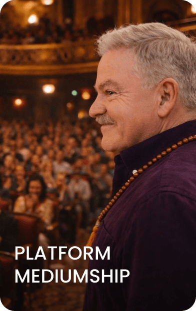 A man wearing a beaded necklace stands on stage, smiling, in front of an audience in a theater. Text on the image reads "Platform Mediumship.